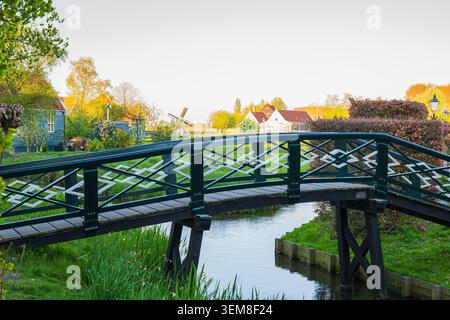 Niederländische Windmühle und traditionelle Brücke über den Wasserkanal im authentischen Dorf Zaanse Schans, holländische Landschaft mit historischem hölzernem Ho Stockfoto