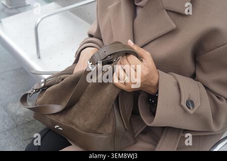 Frau sitzt und hält eine braune Tasche auf einer Bank Stockfoto