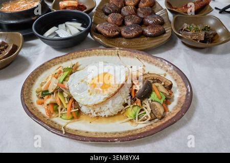 Reis mit Spiegelei und gebratenen Shiitake-Pilzen, serviert mit traditionellen Beilagen auf einer rustikalen Keramikplatte. Stockfoto