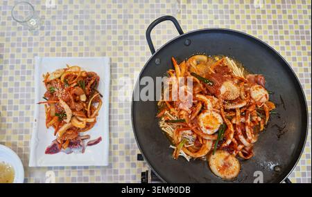 Blick von oben auf koreanische, scharfe, einheimische Hühnchen-Bulgogi in einer Pfanne, serviert mit rohem Hähnchensalat und roter Chili-Sauce auf einem gefliesten Tisch. Stockfoto