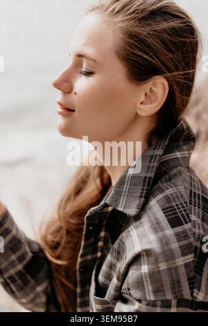 Frau Profil Kontemplation eine ruhige junge Frau mit geschlossenen Augen, die draußen ein graues Flanellhemd in natürlichem Licht trägt Stockfoto