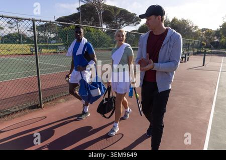 Verschiedene Tennismannschaftskameraden, die auf dem Hardcourt entlang laufen und Schläger, Duffels und Handtücher tragen Stockfoto