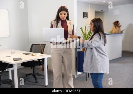 Zwei weibliche Kollegen im mittleren Erwachsenenalter, die den Laptop-Bildschirm im Büro in Geschäftskleidung mit Notebook überprüfen Stockfoto