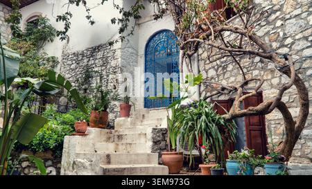 Marmaris, Türkei - 4. April 2026: Traditioneller mediterraner Innenhof mit Steinmauern, weiß getünchten Stufen, blauem Eisentor und tropischen Pflanzen Stockfoto