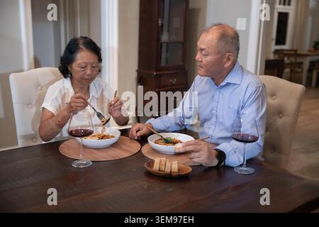 Asiatisches Ehepaar ältere Frauen und Männer mittleren Alters teilen sich Pasta mit Brot zu Hause und trinken Rotwein Stockfoto