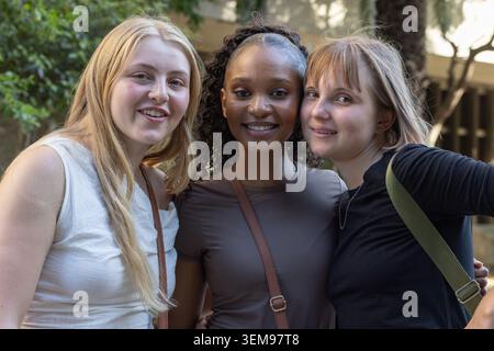 Verschiedene Freundinnen posierten und lehnten sich hinein, lächelten mit Crossbody-Riemen zur Kamera im Innenhof Stockfoto