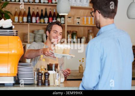 Barista, Kaffee und Take-away-Bestellung mit Mann im Café für Abholung, Gastfreundschaft oder Service. Schenken, lächeln und mit dem Kellner gehen, der Gäste bei bedient Stockfoto