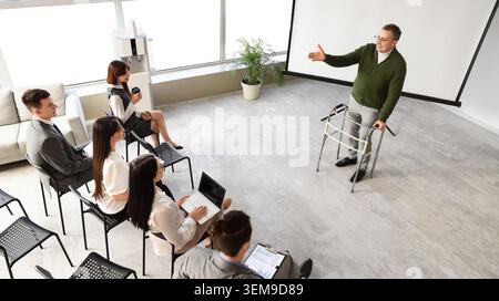 Leitender Geschäftsmann mit Walker, der Kollegen im Besprechungsraum des Büros vorstellt, einschließlich Seminar am Arbeitsplatz und professionelle öffentliche Rede Stockfoto