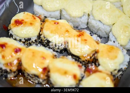 Frische Makizushi-Sushi-Brötchen mit reichhaltiger cremiger, würziger Sauce und bestreuten schwarzen Sesamsamen, aufgenommen in sanfter natürlicher Beleuchtung mit flachem Fokus Stockfoto