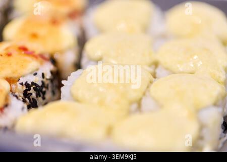 Makroansicht von Makizushi-Sushi-Brötchen mit cremiger Sauce und schwarzen Sesamsamen auf neutralem Hintergrund mit sanften hellen Tönen Fokus auf Front-Sushi Stockfoto