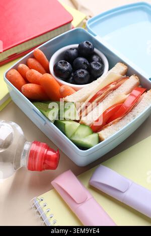 Lunchbox mit leckerem Essen, Wasser und Schreibwaren auf beigem Hintergrund, Nahaufnahme Stockfoto