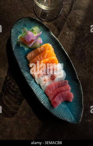 Eine Hochwinkelaufnahme einer frischen Auswahl von Sashimi, einschließlich geschnittenem Lachs, Thunfisch, Weißfisch und Lachsrogen, garniert mit einer Orchideenblüte auf einem Tex Stockfoto