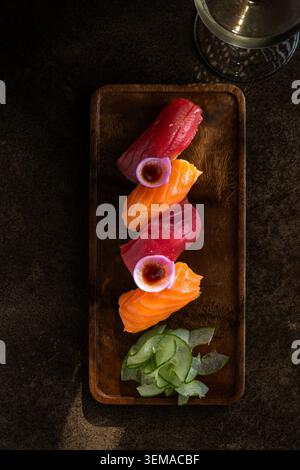 Eine vertikale Aufnahme einer Vielzahl von Lachs- und Thunfisch-Nigiri-Sushi-Stücken, die wunderschön mit Rettichgarnituren und Gurkenscheiben auf einem Rusti angeordnet sind Stockfoto