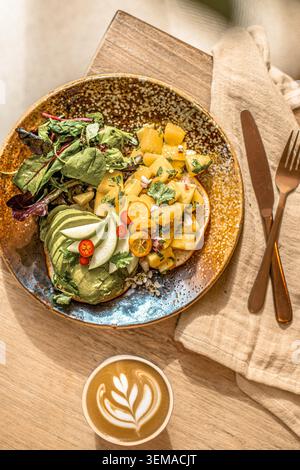Ein Blick von oben auf Toast mit offenem Gesicht mit Mangosalsa, Kumquat und Avocado, serviert mit einem Beilagensalat und einem heißen Tulpenlatt. Stockfoto