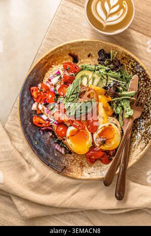 Ein Blick von oben auf Sauerteig Toast mit frischen, traditionellen Tomaten, Basilikum und marmelierten, weich gekochten Eiern, serviert mit Salat und einem Latte. Stockfoto
