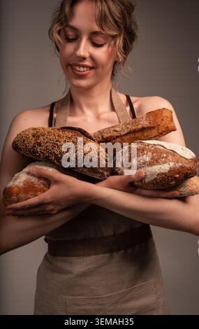 Bäckerin hält frisch gebackene Brotlaibe und zeigt eine Vielzahl von rustikalen Bio-Vollkornprodukten Stockfoto