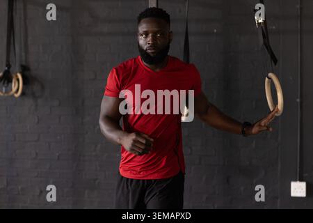 Afroamerikaner mit rotem Hemd und schwarzen Shorts, die Hand auf einem Holzring im Fitnessstudio Stockfoto