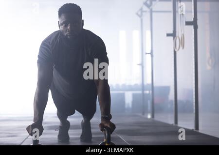 Afroamerikanischer Mann, der Liegestütze auf parallettes in einem kommerziellen Fitnessstudio mit Rig und Ringen macht Stockfoto