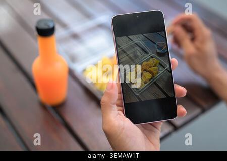 Ein Nahaufnahme, Landschaftsfoto aus einem hohen Blickwinkel, das auf ein pinkfarbenes Smartphone in der Hand einer Person fokussiert. Auf dem Telefonbildschirm wird ein helles, Stockfoto
