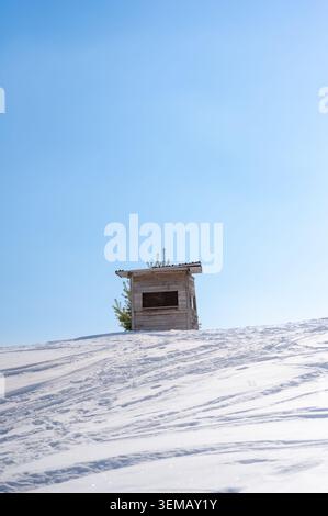 Kleine Holzhütte auf einem schneebedeckten Hang bei Birgitzköpfl in Tirol, Österreich, unter klarem blauem Winterhimmel. Stockfoto