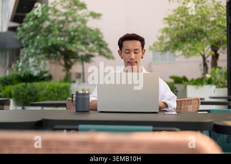 Ein breit angelegtes Geschäftsporträt eines nicht binären, geschlechtsorientierten thailändischen schwulen Mannes aus der Region Isan, der sich auf einen silbernen Laptop konzentriert. Er ich Stockfoto