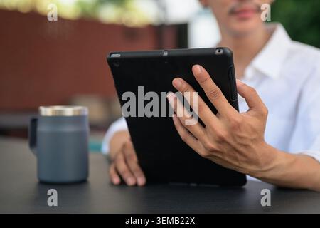 Ein horizontales Nahfoto, das sich auf eine Hand konzentriert, die ein schwarzes digitales Tablet in einem Büro im Freien hält. Die Kamera fokussiert auf die Textur von Th Stockfoto