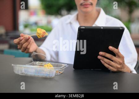 Ein horizontales Nahaufnahme-Foto mit Fokus auf eine Hand-in-Frame-Perspektive einer Person, die Technologie und Mittagessen an einem Ort im Freien verwaltet. Die Rahmenkappe Stockfoto