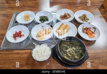 Traditionelles koreanisches Gericht mit getrockneter Rettich-Grünsuppe in einem Tontopf, weißem Reis und verschiedenen authentischen Beilagen auf einem Holztisch. Stockfoto