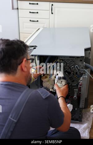 Fachkundiger Servicetechniker, der einen geöffneten Geschirrspüler instand setzt und interne Komponenten und elektrische Anschlüsse für die Gerätereparatur überprüft. Stockfoto