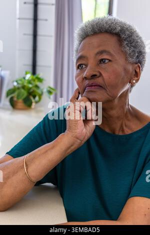 Ältere Afrikanerin trägt ein blaues Oberteil, das Kinn auf der Hand liegend, und sie blickt auf die heimische Arbeitsplatte Stockfoto