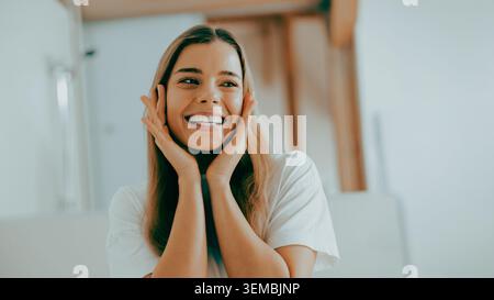 Glückliche junge Erwachsene kaukasische Frau lächelt und berührt ihr Gesicht in einem hellen Badezimmer Stockfoto