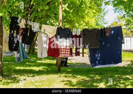 Nasse bunte Kleidung, die an Seilen im Freien hängt, mit Plastiktüchern in einem grünen Garten, natürlichen umweltfreundlichen Wäschetrocknungslösungen und dom Stockfoto