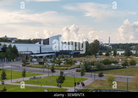 HELSINKI, FINNLAND - 11. AUGUST 2025: Großer Panoramablick auf einen modernen Stadtkomplex mit grünen Rasenflächen und Bäumen unter einem dramatisch bewölkten Himmel. Stockfoto