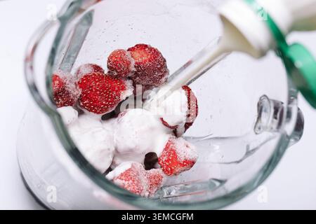 Gefrorene Erdbeeren, gemischt mit Milch in Glaskanne. Gesunde Smoothie-Vorbereitung Hintergrund für hausgemachte Getränke Frühstück und frische Obst Rezepte. Stockfoto