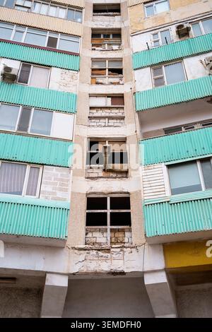 Verwitterte Wohnblockfassade aus der Sowjetzeit mit türkisfarbenen Wellbalkonen und beschädigten Fenstern, die städtische Wohnarchitektur in Uzbekis zeigen Stockfoto
