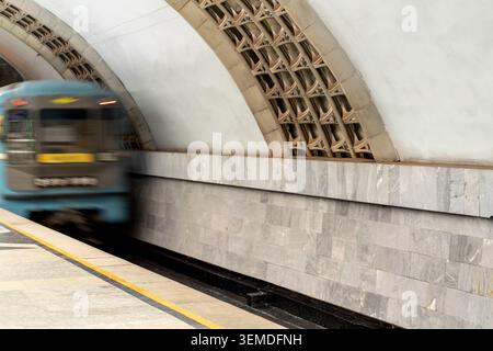 Eine U-Bahn fährt durch die einzigartige Architektur einer U-Bahn-Station in Taschkent, Usbekistan. Die gewölbten Decken und die gefliesten Wände spiegeln sich wider Stockfoto