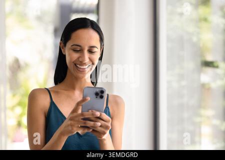 Frau liest Nachricht auf Smartphone im sonnendurchfluteten Wohnzimmer Stockfoto