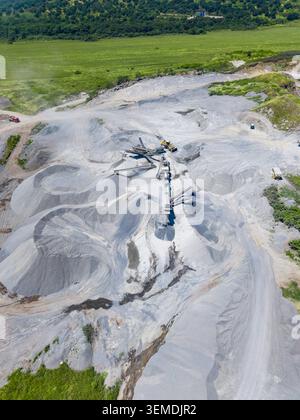 Ein Granitsteinbruch weist große Granitsteinfelsen und schwere Maschinen auf. Die Aussicht ist von oben, zeigt das weite Land und die Aktivitäten während Stockfoto
