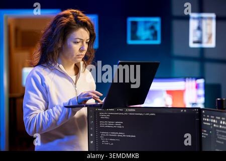 IT-Systemadministrator führt Software-Debugging mit Laptop durch und überprüft Fehler in Codezeilen, die auf Desktop-PC-Monitoren angezeigt werden. Frau, die zu Hause im Büro steht und Codierungsprobleme mit dem Notebook behebt Stockfoto