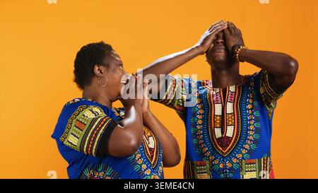 Fröhliches afroamerikanisches Paar lacht über die Sache im Studio, hat Spaß mit Witzen und amüsiert über den Hintergrund. Verheiratete ethnische Leute, die vor der Kamera lachen, fröhliche Partner. Stockfoto