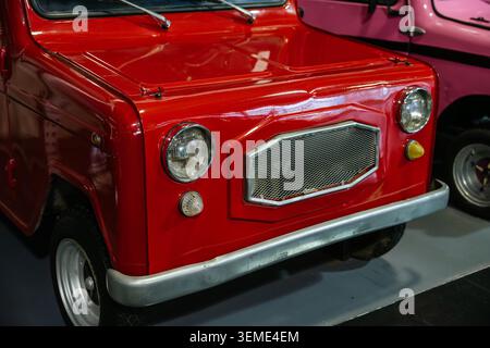 Die Nahaufnahme macht ein leuchtend rotes Oldtimerauto aus einem niedrigen Winkel. Glänzender Stoßfänger aus Chrom und strukturierter Kühlergrill unterstreichen das klassische Design mit einem rosafarbenen V Stockfoto