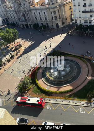 Erhöhter Blick auf die Plaza del Ayuntamiento in Valencia, Spanien, mit Brunnen, Fußgängern und einem roten Stadtbus. Stockfoto