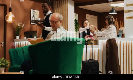Alte Frau, die Anmeldeformulare an der Rezeption ausfüllt, das Zimmer beim Check-in vorbeigeht und sich auf den Start des Ruhestandurlaubs vorbereitet. Der Reisende fragt an der Rezeption nach All-Inclusive-Service. Handgeführte Aufnahme. Stockfoto