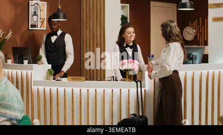 Weibliche Kundin checkt in der luxuriösen Hotellobby mit Hilfe des freundlichen Concierge-Personals ein. Der Rezeptionist begrüßte eine ältere Frau an der Rezeption und half bei der Anmeldung. Handgeführte Aufnahme. Stockfoto