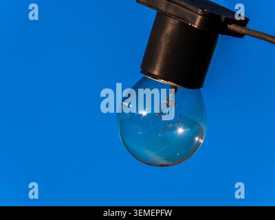 Hochwertige Glühlampe für den Außenbereich, die an einem Draht hängt. Diese minimalistische Komposition besteht aus einer transparenten Glühlampe und einer leuchtenden Clea Stockfoto
