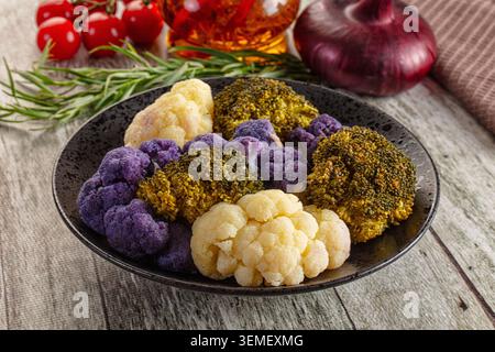 Großaufnahme von violettem Blumenkohl, weißem Blumenkohl, Brokkoli-Röschen auf einem rustikalen dunklen Teller mit Kirschtomaten, roten Zwiebeln, Rosmarin auf einem Holz Stockfoto