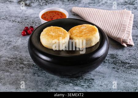 Goldene gebratene Käsepfannkuchen, Syrniki-Hüttenkäse-Fritter, auf elegantem schwarzen Teller. Leuchtende rote Beerensauce, frische Preiselbeeren, hellrosa strukturiert n Stockfoto
