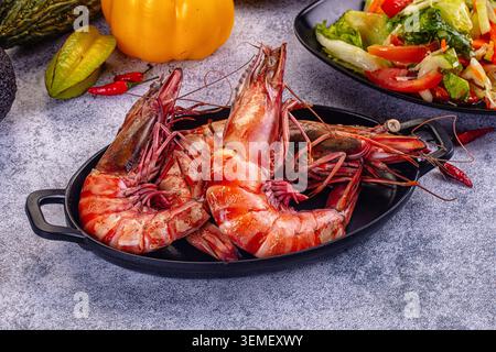Große gegrillte Tigergarnelen auf einem schwarzen ovalen Teller, begleitet von frischem Gemüsesalat, gelbem Paprika, Sternfrüchten und rotem Chili Stockfoto