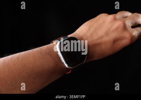 Nahaufnahme eines Mannes, der eine moderne quadratische Smartwatch mit leerem schwarzen Bildschirm trägt, technisches Konzept auf schwarzem Hintergrund. Stockfoto