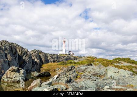 Cape Forchu Lighthouse über zerklüfteten Küstenfelsen in Yarmouth Nova Scotia Kanada mit dramatischen Wolken, blauem Himmel und reflektierenden Gezeitenbecken Stockfoto